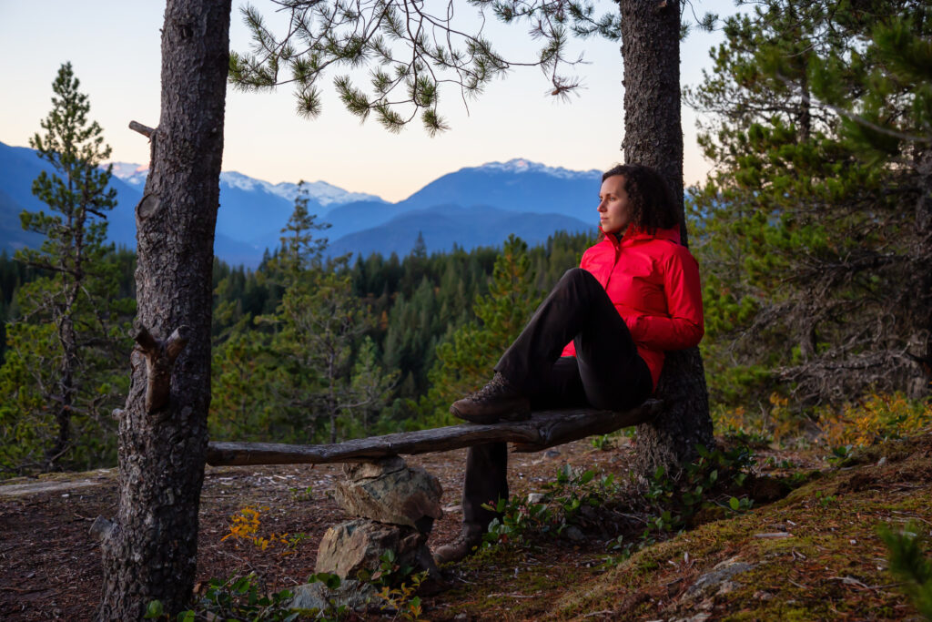 Kvinne nyter stillheten på en benk med utsikt over barskog.