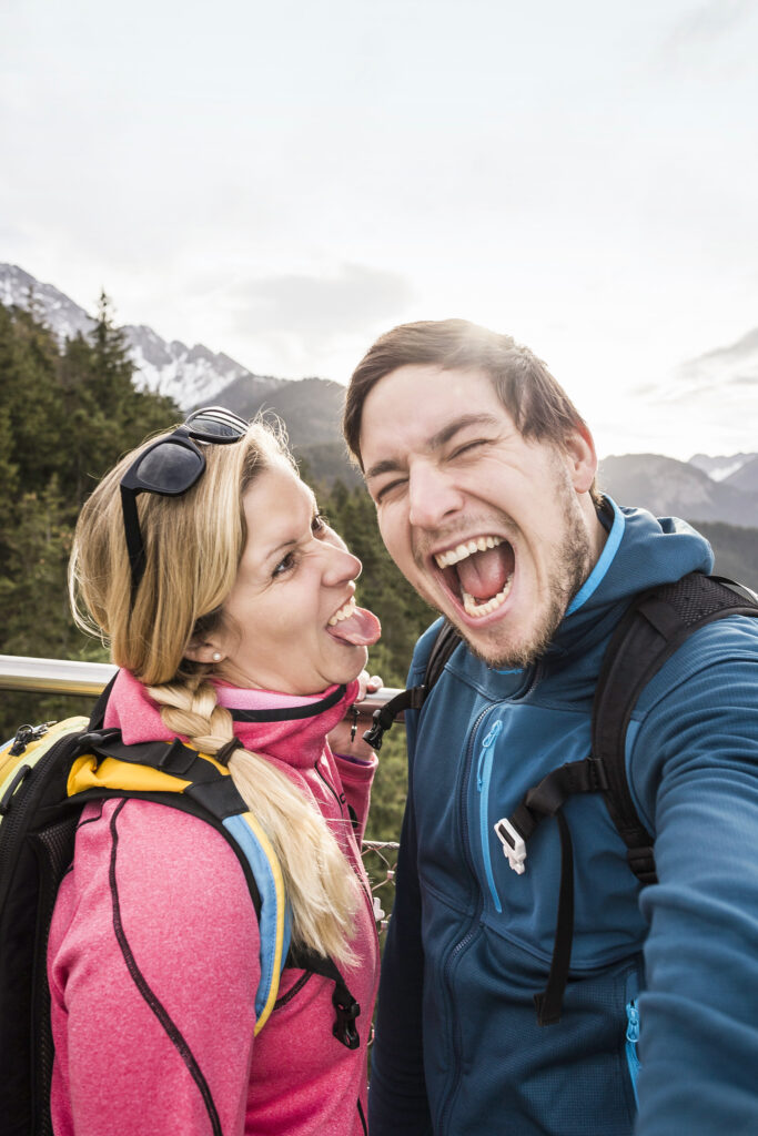 Selfie mann og kvinne som lager grimaser, på tur med fjellet i bakgrunn.
