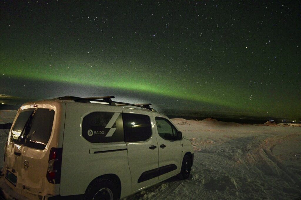 Campingbil i vinterlandskap om natten under en mørk himmel med nordlys.