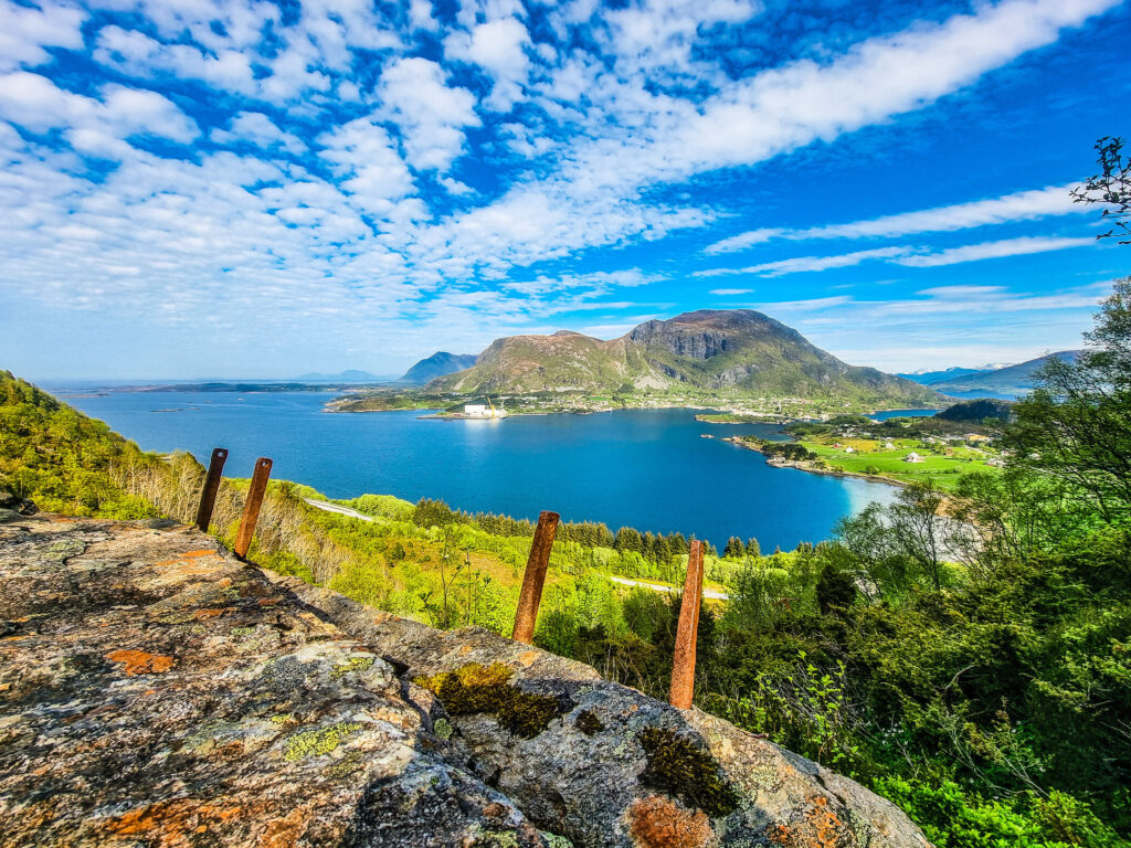 Panorama av Stordalsvatnet. Blå himmel, blått vann, sol og grønt fjellandskap.