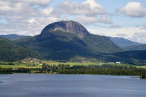 Andersnatten i Sigdal kommune. Omgitt av skog. Blått, stille vann i forgrunnen under en blå lett overskyet himmel.