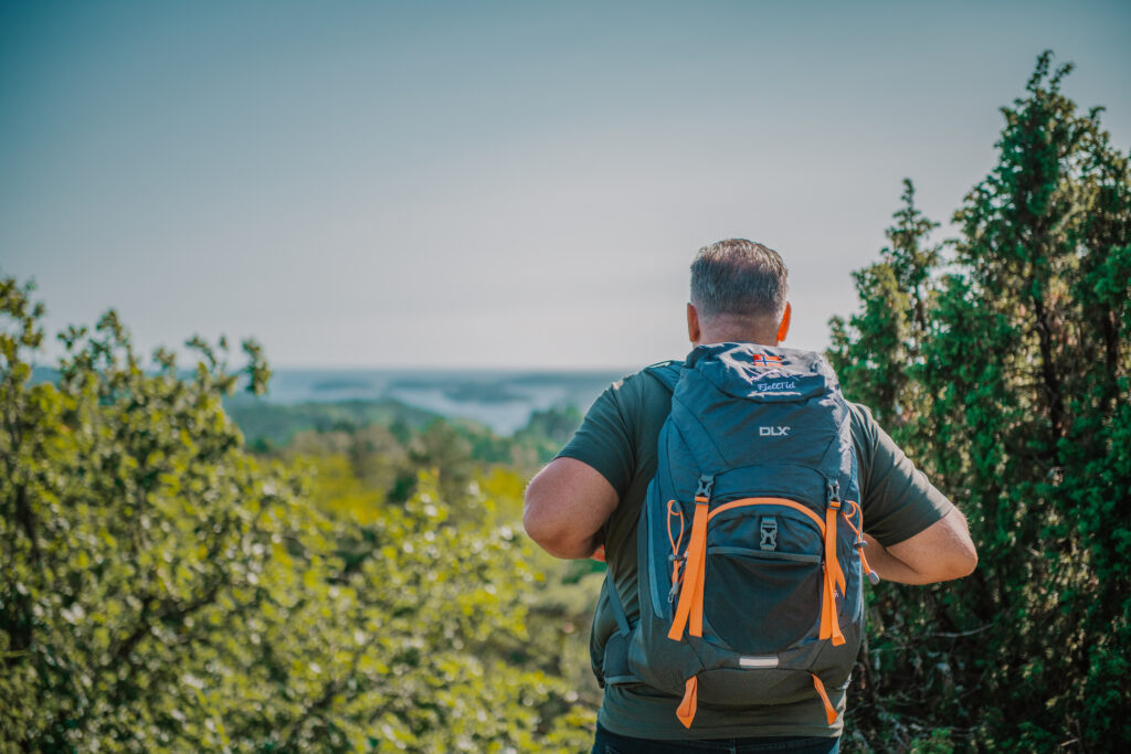 Mann med fjelltidsekken, i skog med utsikt.