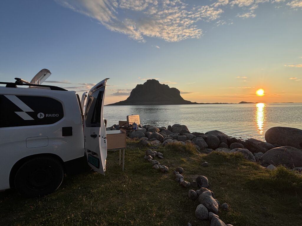 Solnedgang på Sundvolden, på øya Vega. Campingbilen, med hav og en øy i bakgrunn. Og oransj midnattsol i horisonten.