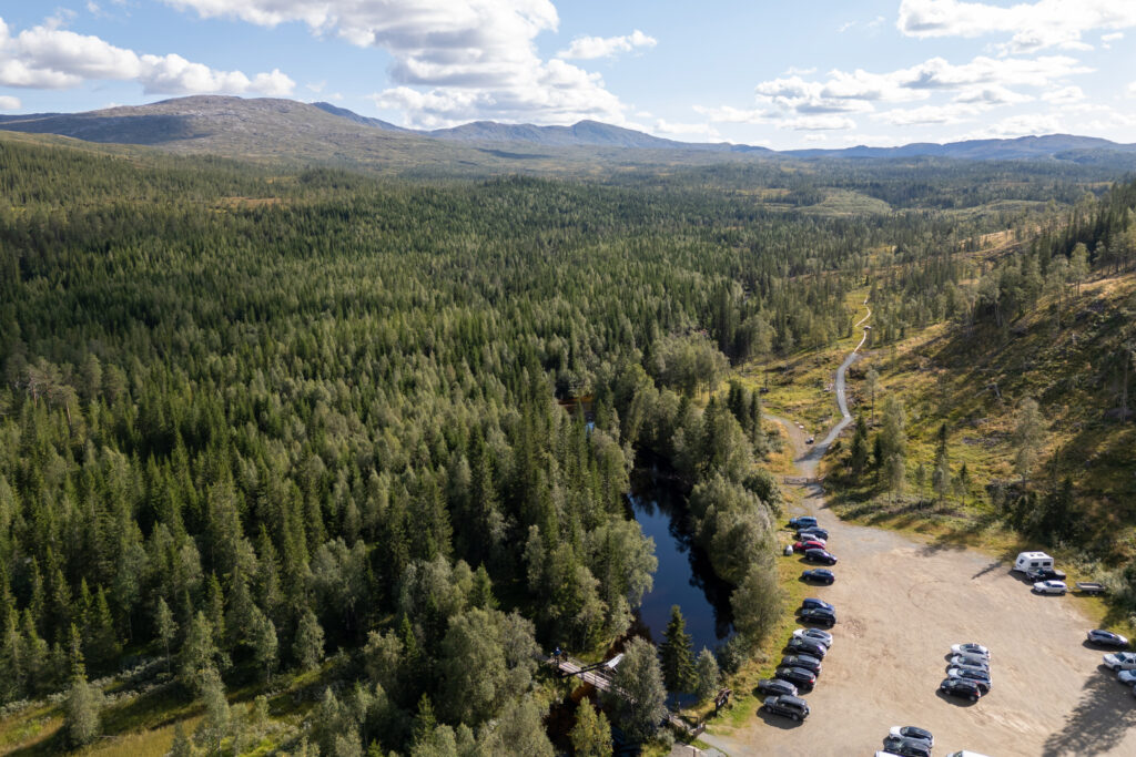 Utsiktsbilde over skogdekt landskap med en parkeringsplass nederst i høyre hjørne.