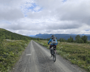Tour de dovre. Sykkeltur over Dovre. Syklist på grusvei omgitt av vakkert fjellandskap.