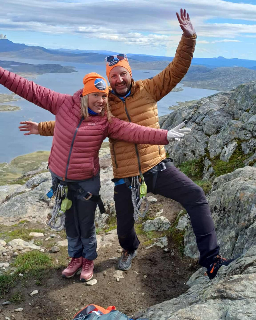 To glade turdeltakere i fjellet poserer mot kamera med spektakulær utsikt i bakgrunn.