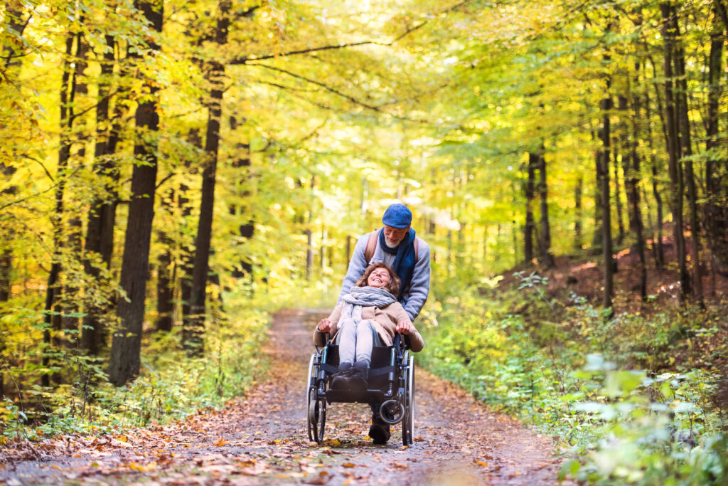 Senior couple with wheelchair in autumn forest.