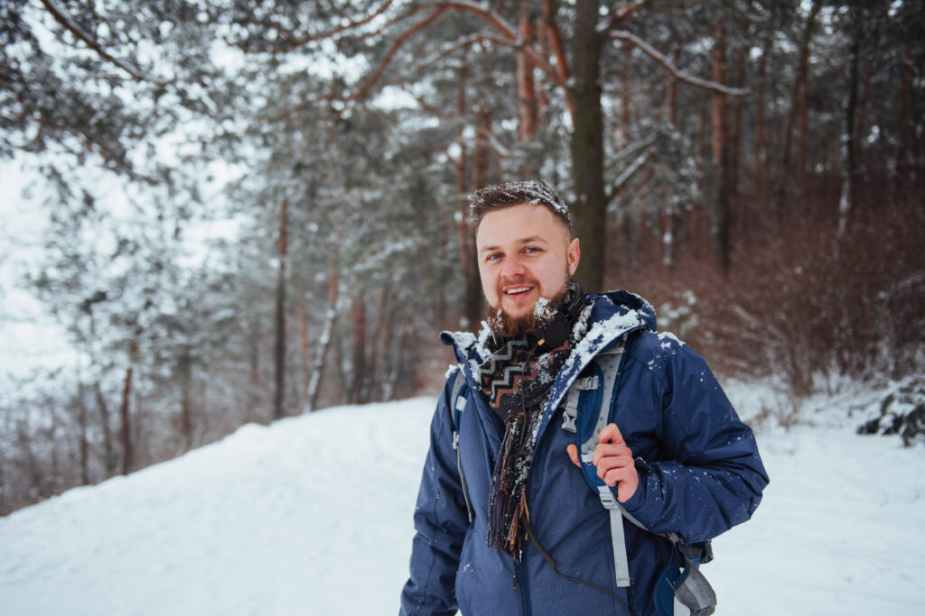 Man Traveler with backpack hiking Travel Lifestyle adventure concept active vacations outdoor. Beautiful landscape with forest of coniferous trees and white snow.
