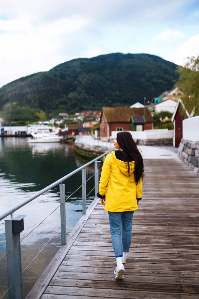 Young woman enjoys picturesque landscape. The girl tourist in a yellow jacket posing in the Norway.